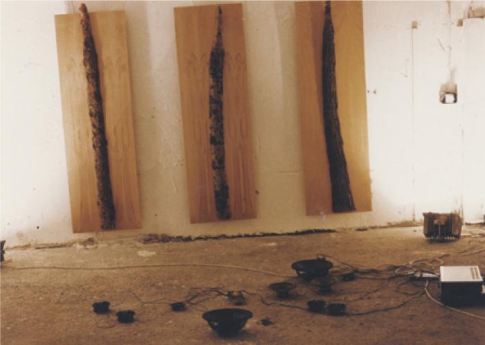 1992. november 25–27. Az Újlak Csoport tagjainak közös kiállítása harmadik működési helyszínükön, a Tűzoltó utca 72.-ben. Ravasz András Messiaen installációja. A terem falára három, rétegelt lemezre applikált fakérget szerelt ferdén, kissé megbillentve a teret. A négy sarokban négy felfelé fordított reflektor világított. A padlón elszórt magas és mély hangszórókból Olivier Messiaen Méditation sur le mystère de la Sainte Trinité c. műve szólt. © Fotó: Farkas Gábor